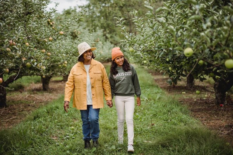 An older person holding hands with a younger person walking in an apple orchard.