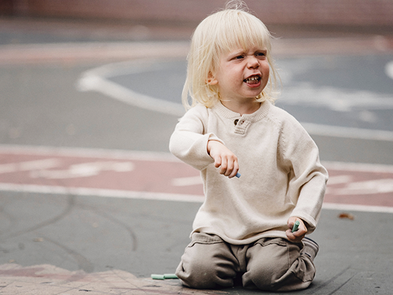 a toddler with an angry face kneeling on a playground