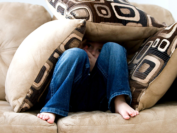 a middle schooler hiding under a fort of couch cushions