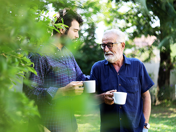 A younger man and an older man outside drinking coffee