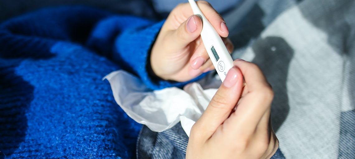 Person in a blue sweater holding a thermometer and tissue