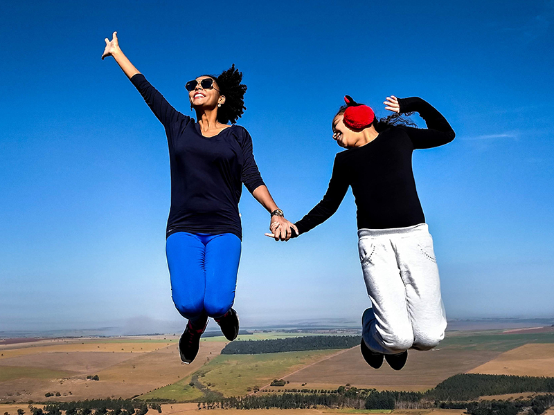 Two women jumping in the air with a blue sky behind them.