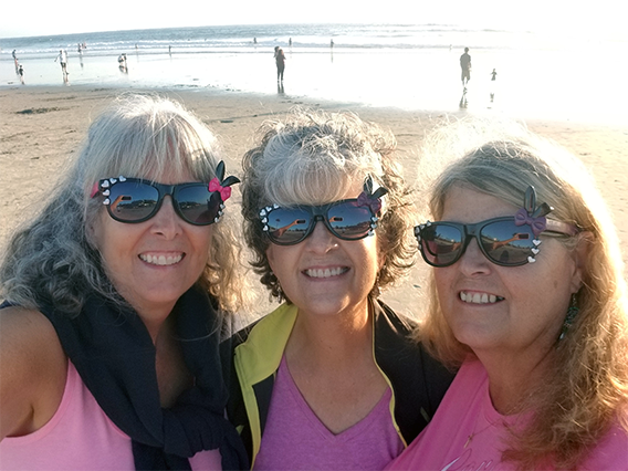 three women on a beach wearing sunglasses and pink shirts