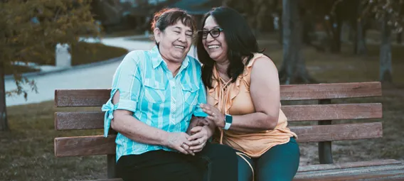 two women sitting on a bench in a park laughing and smiling