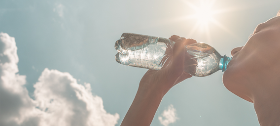 background of a blue sky and sun with a person drinking from a water bottle in front
