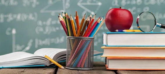 Desk with book, apple, pencils and books with chalkboard in the background