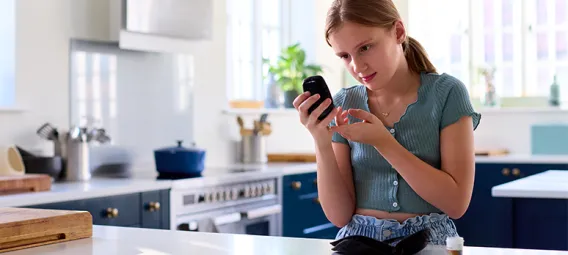 Diabetic Girl At Home Testing For Blood Glucose Level With Monitor Kit In Kitchen