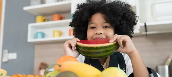 Happy child girl eating watermelon in the kitchen. 