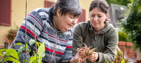 a caregiver explains to a mentally handicapped woman how to mulch with straw