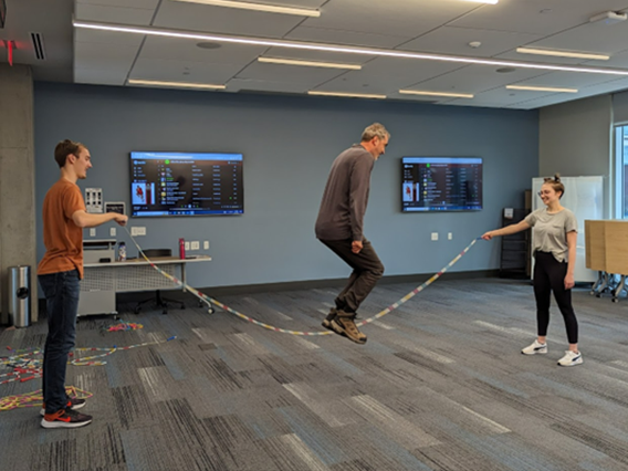 Two colleagues move the jump rope while a male colleague jumps in the middle