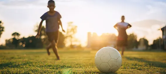 Silhouette action sport outdoors of a group of kids having fun playing soccer football for exercise and recreation at the green grass field under the twilight sunset sky.