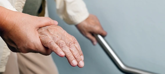 A close-up of a younger person gently holding the hand of an elderly individual who is gripping a metal handrail, offering support and care.