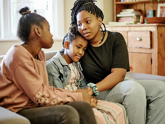 "Mother having a caring conversation with two children on couch in comfortable home setting, showing family support and communication