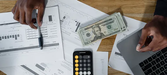 Top view of a desk with papers, financial statements, money and a calculator