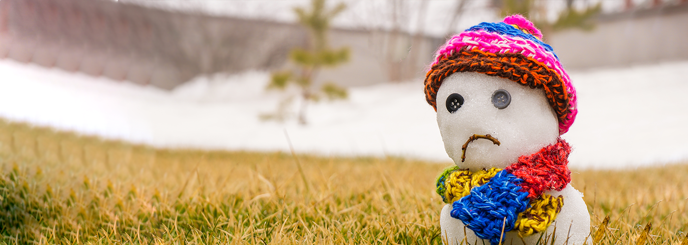 A snowman with a sad face wearing a knit hat and scarf
