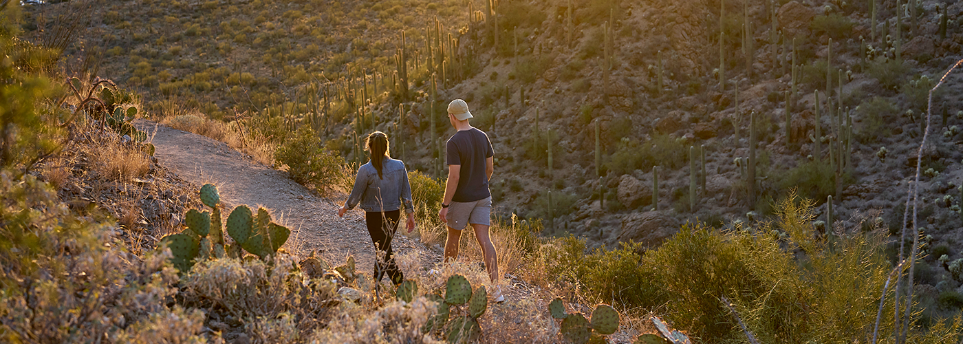 two people walking down a path through the arizona desert