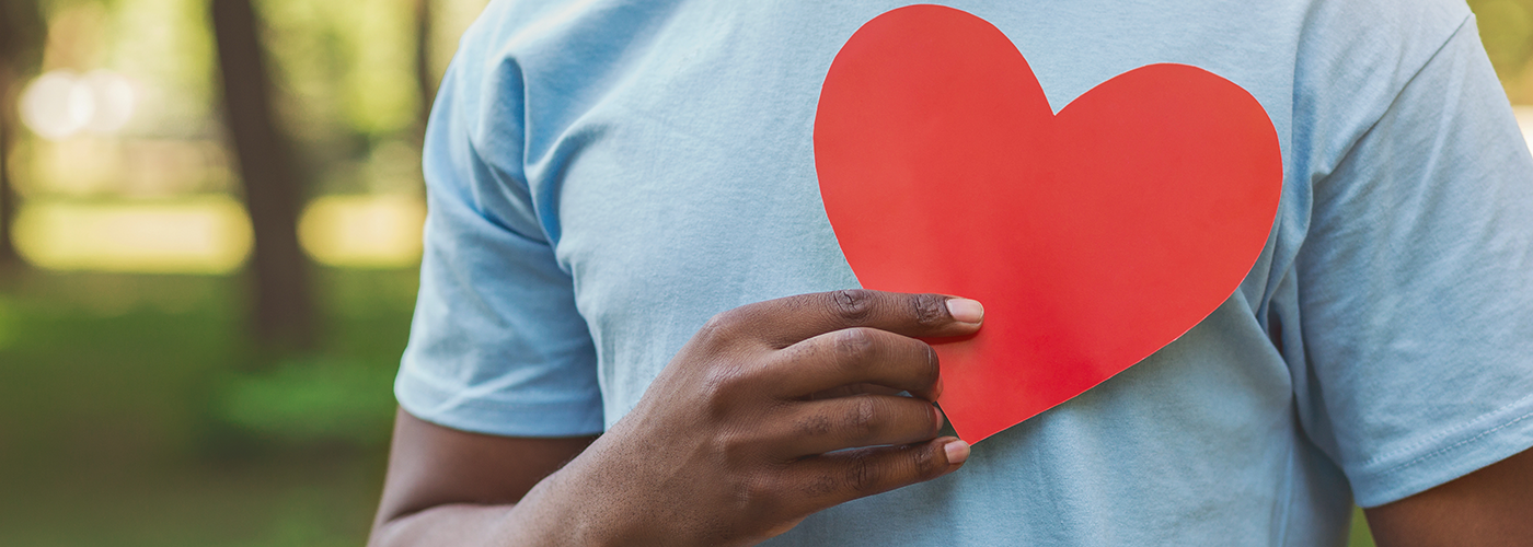 An African American man holding up a red paper heart over this chest.