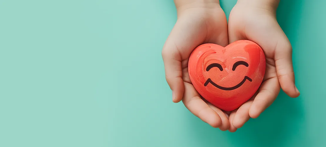 Hand holding a plastic heart with a smiley face on it.