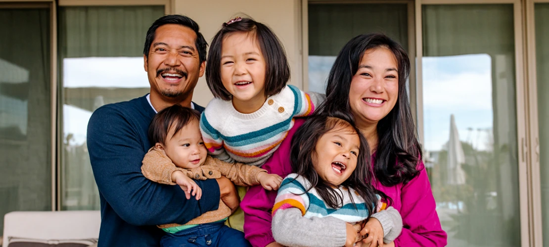 A smiling family of five poses happily in front of a house.