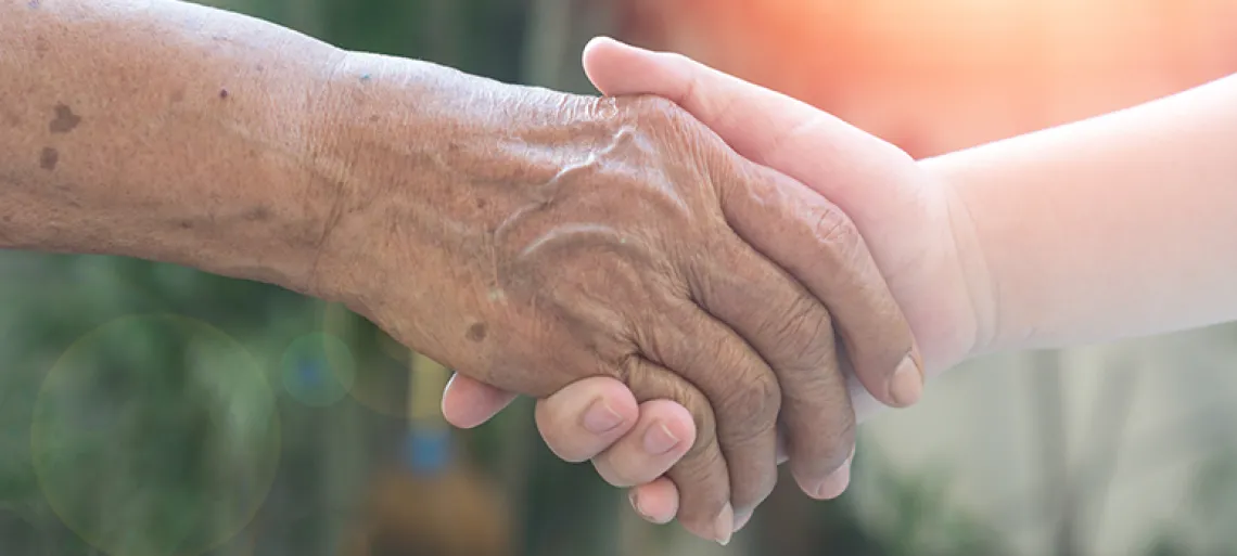 An elder holding the hand of someone younger