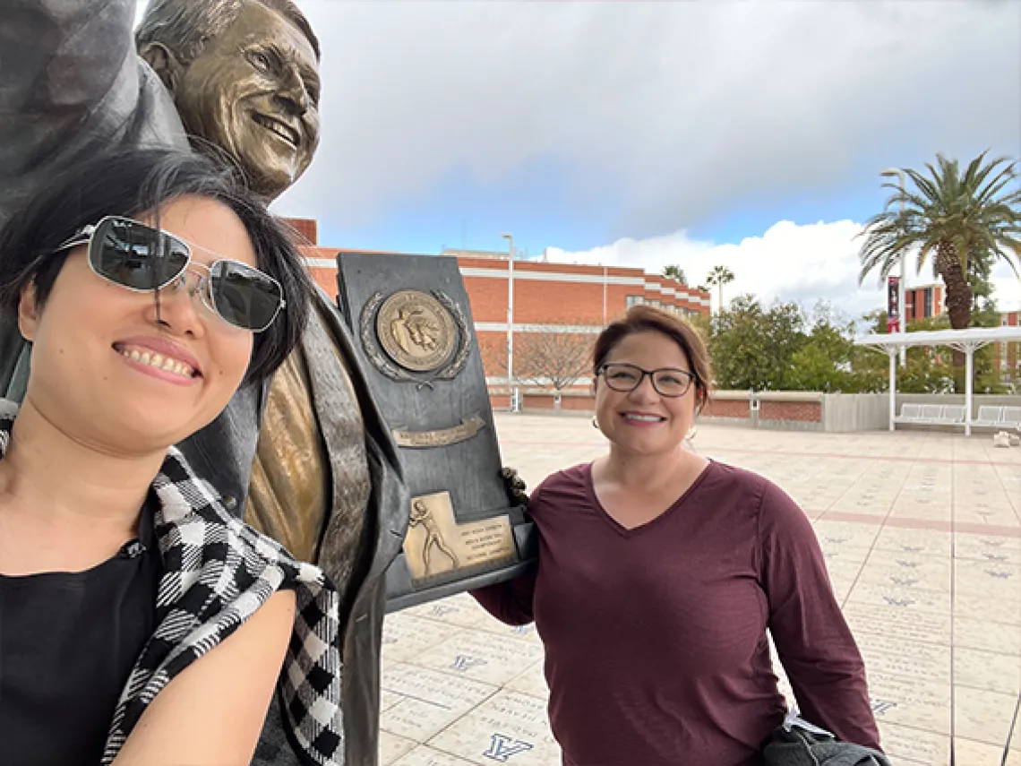 Two smiling women in front of a statue