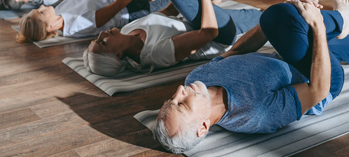 group of senior people stretching in yoga mats in studio