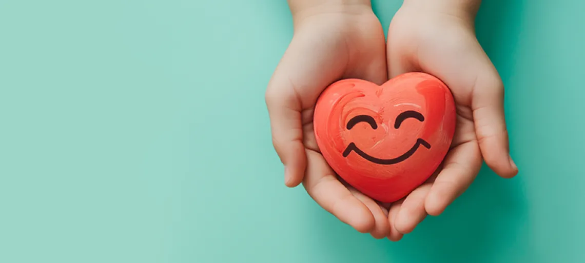 Holding a heart with a happy smiling face on a pale green background