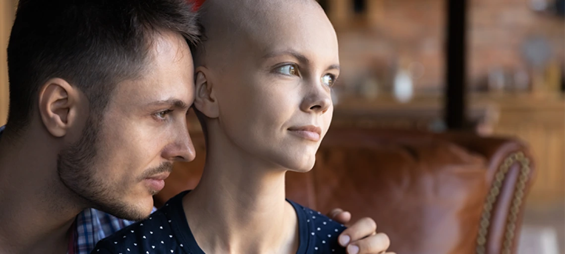 Man embracing and comforting woman who appears to be dealing with cancer or hair loss, showing intimate support and care