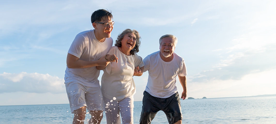 Three generations of family members laughing together while running on beach, showing multigenerational happiness and active aging