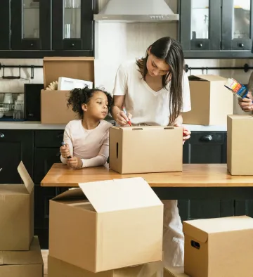 A woman and a child packing up boxes in a kitchen