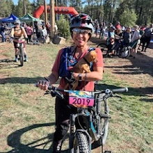 Virginia Ellis on a bike holding a puppy.
