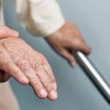 A close-up of a younger person gently holding the hand of an elderly individual who is gripping a metal handrail, offering support and care.