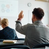 Professional training session with instructor presenting to audience, participant raising hand to ask question in modern classroom setting
