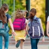 Group of elementary school children with colorful backpacks running together toward school building on a sunny day