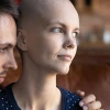 Man embracing and comforting woman who appears to be dealing with cancer or hair loss, showing intimate support and care