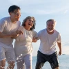 Three generations of family members laughing together while running on beach, showing multigenerational happiness and active aging