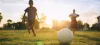 Silhouette action sport outdoors of a group of kids having fun playing soccer football for exercise and recreation at the green grass field under the twilight sunset sky.